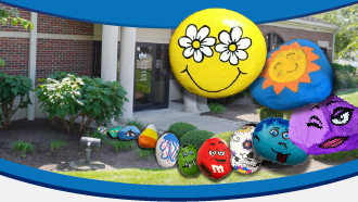 Decorative painted rocks in front of a brick building, featuring a smiley face and sun design.