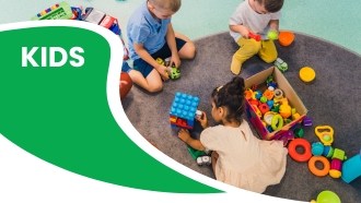 Three children playing with toys on a gray carpet, next to a box of colorful toys.