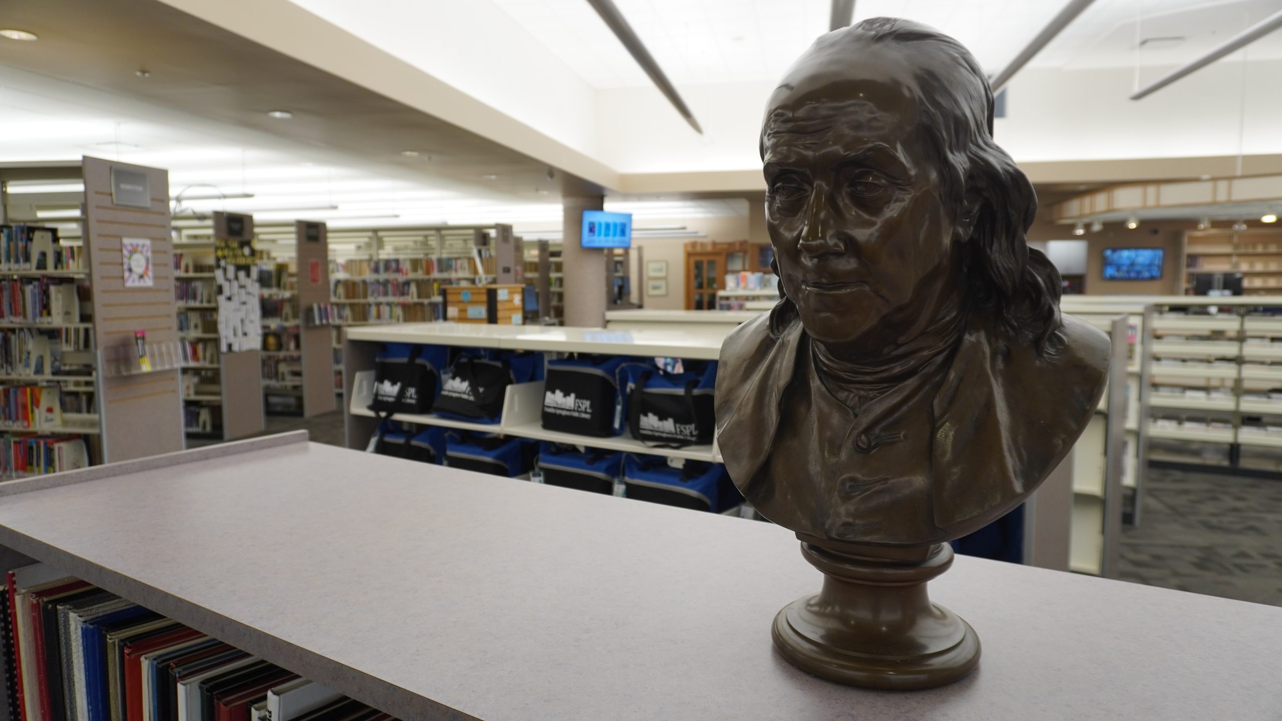Bronze bust in a library with shelves and book kits in the background.
