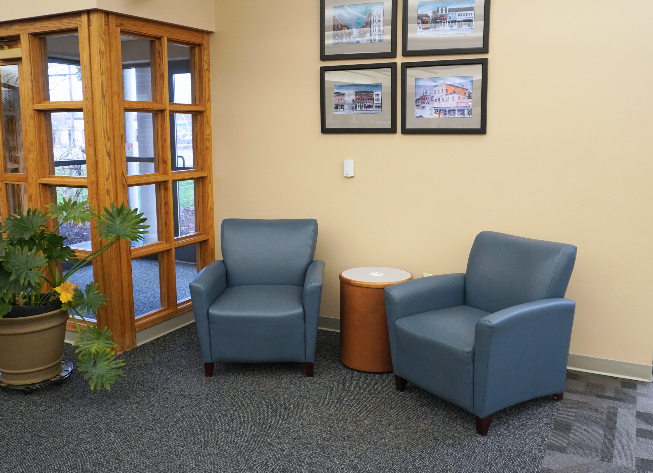 Two blue armchairs and a round table in a seating area with framed photos on the wall.