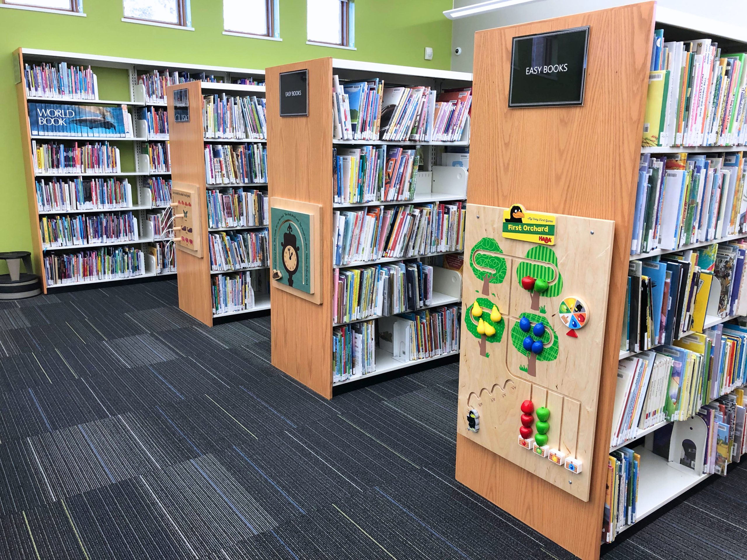 Children's section of a library with bookshelves, colorful books, and interactive wall games.