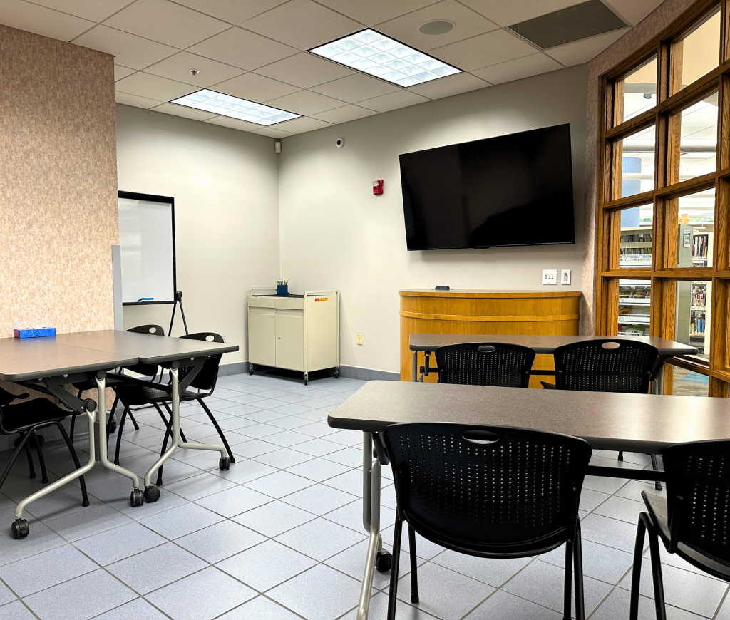 Small meeting room with tables, chairs, whiteboard, and large monitor.