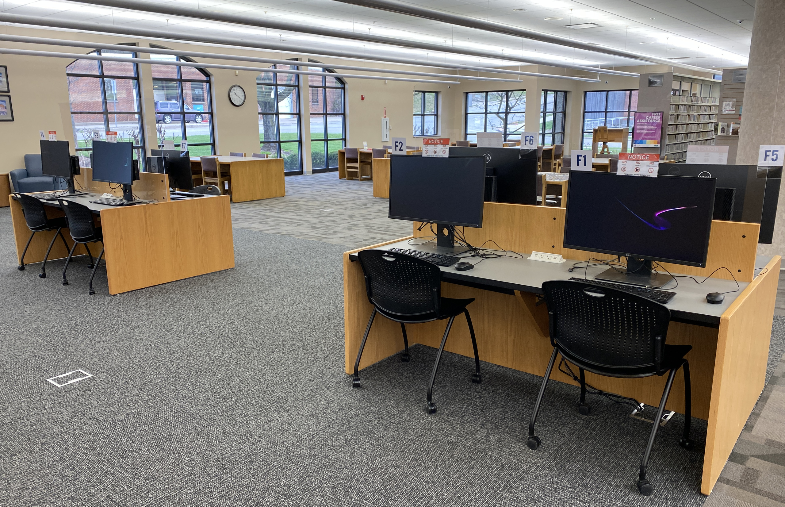 Interior of library with computers, rolling chairs, tables, bookshelves, and windows.